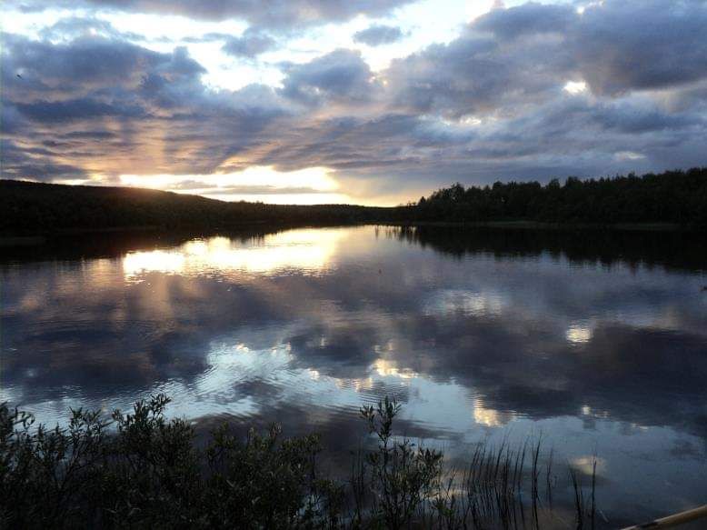 En lugn sjö som speglar molnen på himlen. Solen går ner vid horisonten.