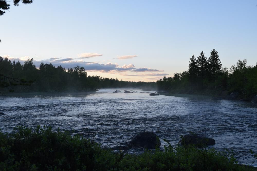 Mist rises from the flowing river. Forest grows along the riverbanks. The sun has set.