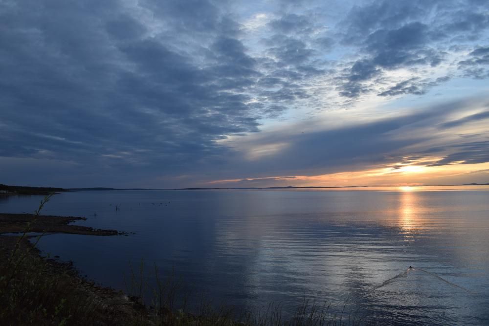 Tyyni järvimaisema auringonlaskun aikaan. Taivas on pilvinen, mutta horisontissa näkyy vielä pilkahdus auringosta.