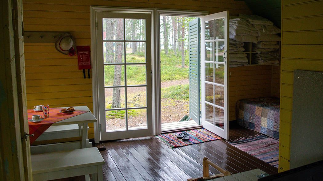 Vasemmassa reunassa ruokapöytä, keskellä ovet ulos, oikessa reunassa puuhella.