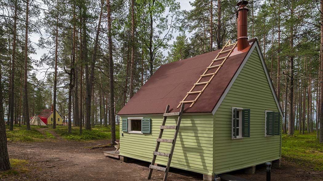 Pieni lautarakenteinen tupa mäntymetsässä lähellä järven rantaa.