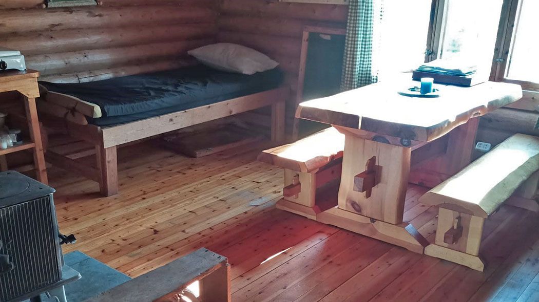 In front of the window, a table, on the left wall a bed. In the foreground you can see the side of a black stove.