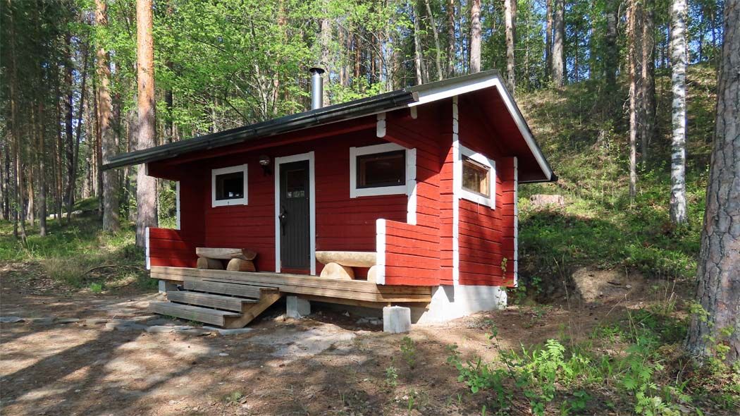 Sauna ulkoa nähtynä. Ulko-oven kummallakin puolella on puinen penkki.