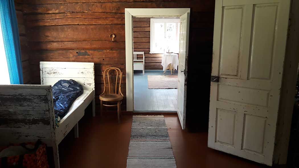 Inside the hut, there is an old wooden bed in the lobby and a chair next to it.