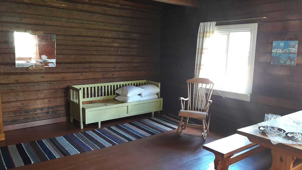 There is a wooden pull-out sofa, rocker chair, dining table and a rug on the floor inside the hut.