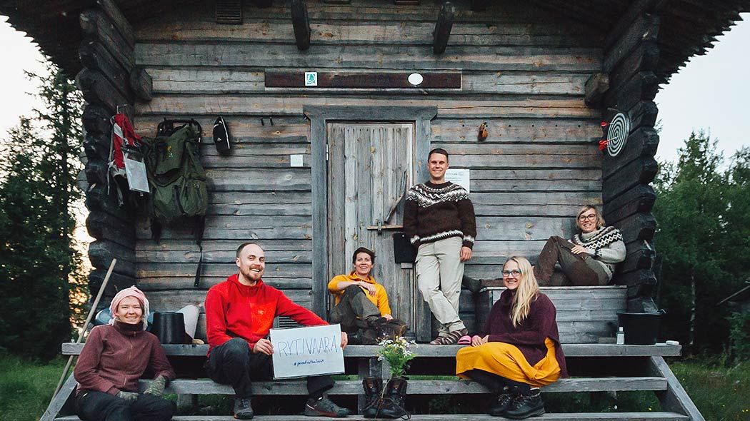 Six happy shepherds pose on the steps of hut in the summer landscape.