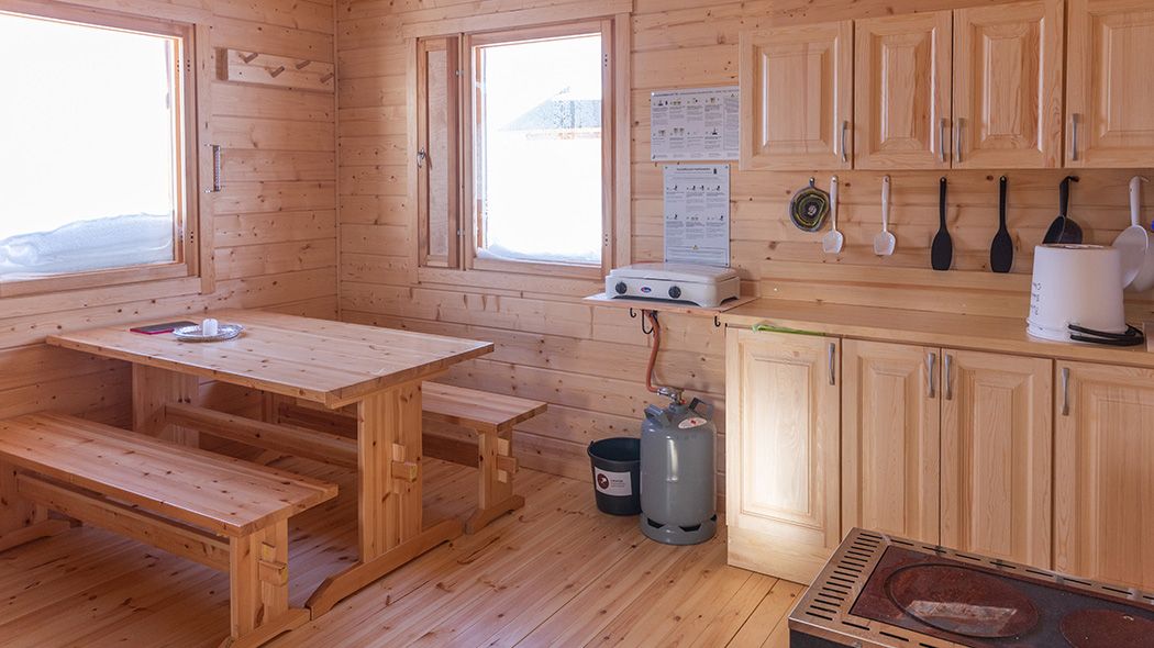 The cottage has a kitchenette, dining table, benches and two windows.