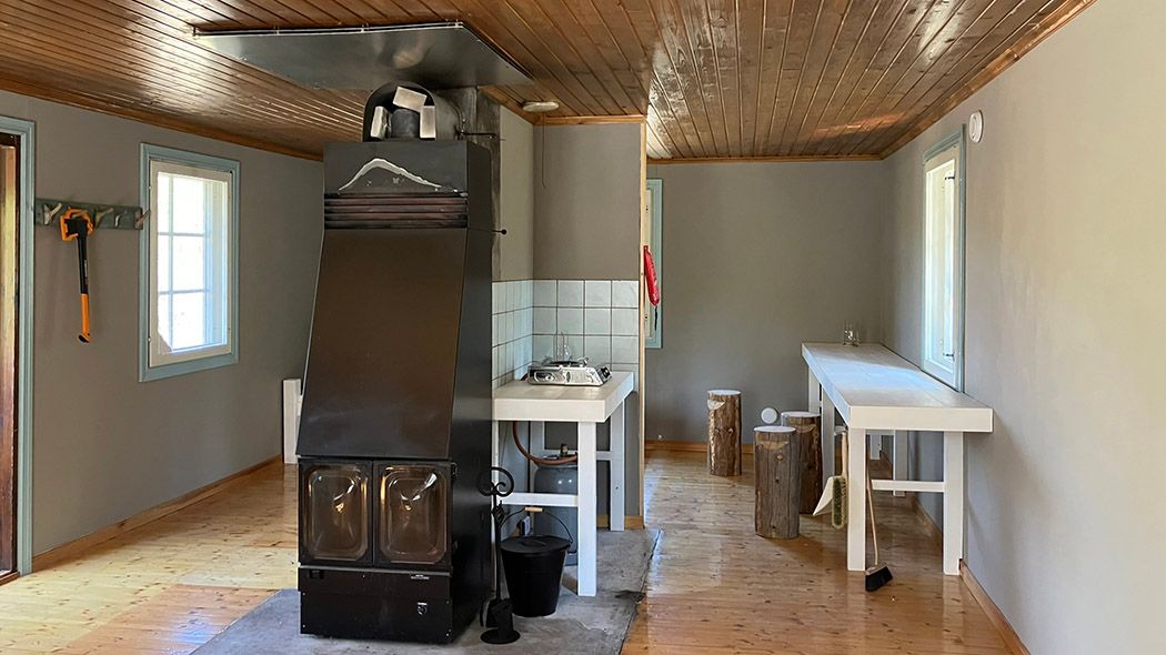Interior view with large fireplace in the centre with glazed doors. Small kitchen space at the back.