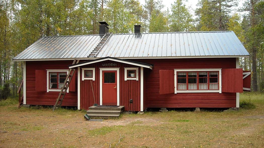 En gammal timmerstuga med texten Uitto ovanför dörren. Stugans fönsterluckor i trä är öppna.
