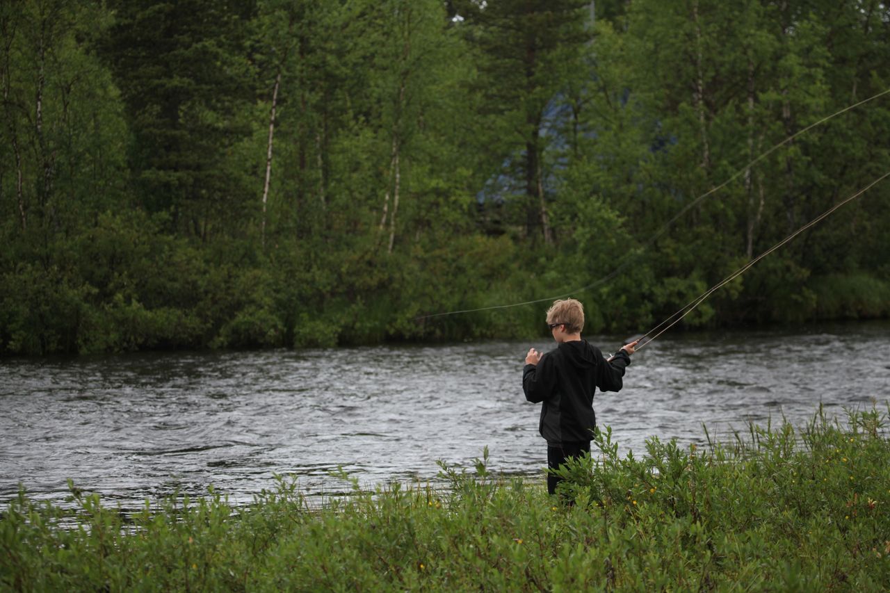 Ett barn står vid floden med ett fiskespö i handen.