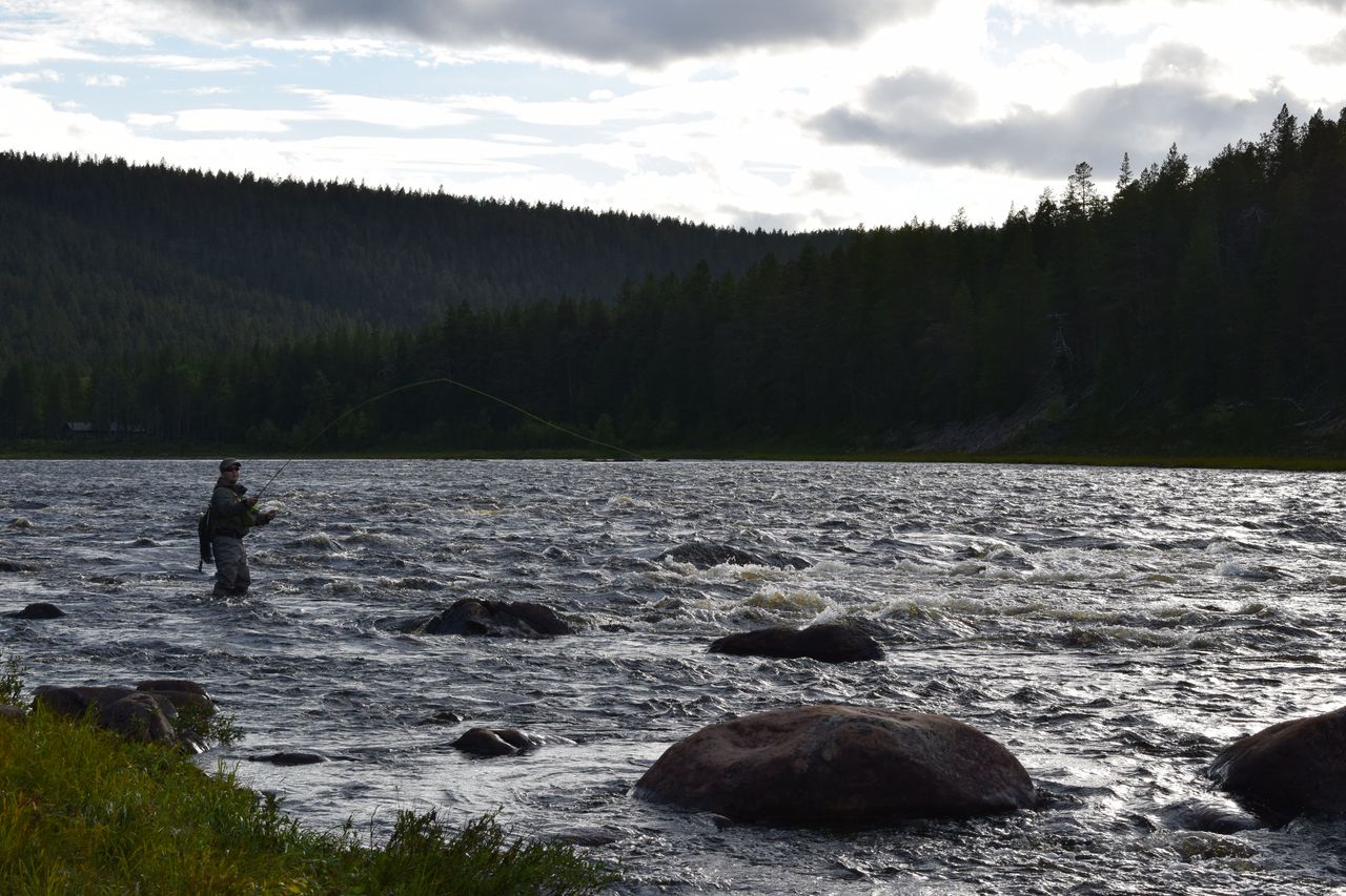 A fisherman stands in a flowing river with a fishing rod in his hand.