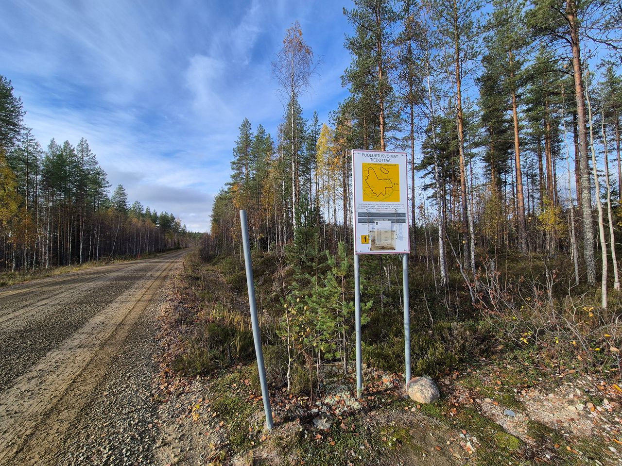 En skogsväg med träd som växer på båda sidor. Det finns en varningsskylt bredvid vägen.