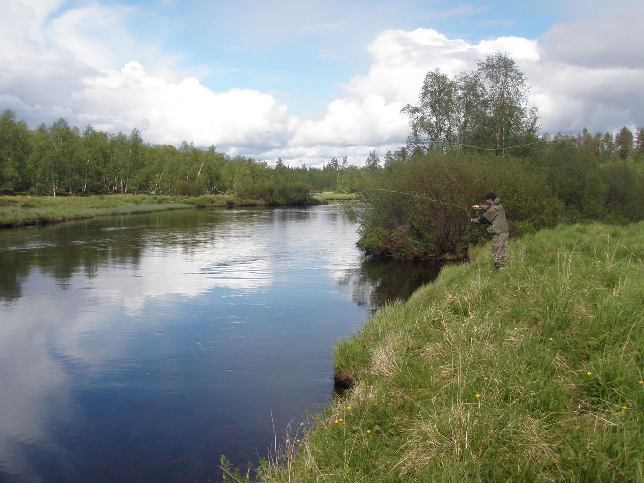 Peilityyni joki. Valkoiset pilvet heijastuvat veden pinnalta. On kesä.