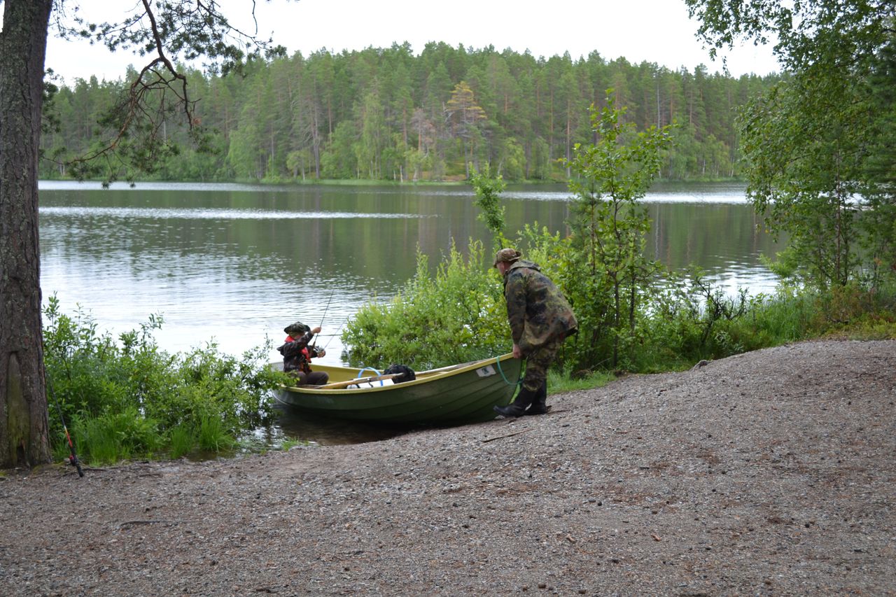 Maastopukuinen mies työntää vesille soutuvenettä, jossa istuu lapsi.