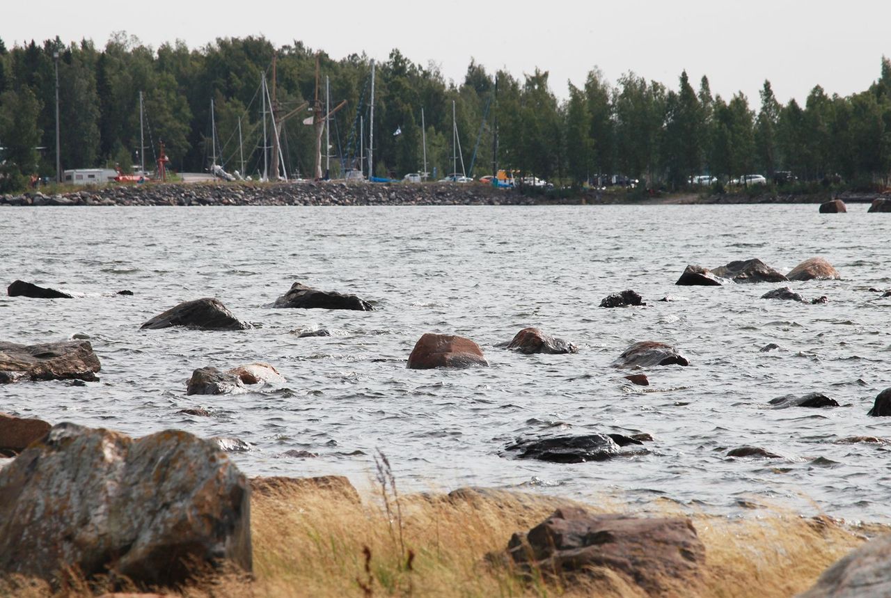Aallokkoinen meri, jonka pinnan rikkoo isot kivet. Taustalla näkyy kalasatama.