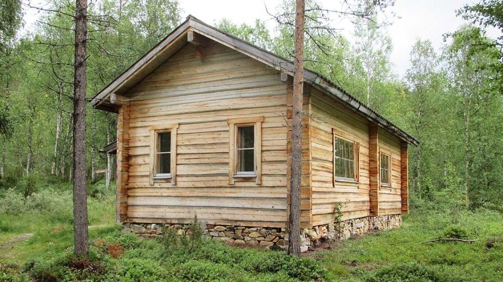 A large log building in the middle of the forest, with two windows on two walls.