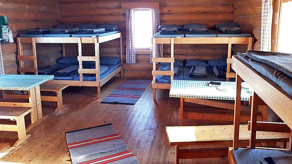 Tuvan päätyseinällä on kaksi leveää kerrossänkyä, joiden välissä on kapea ikkuna. Sängyillä on patjat, tyynyt ja viltit. Molempien kerrossänkyjen edessä on pöytä ja penkit. Etualalla näkyy yhden  kerrossängyn nurkka ja lattialla on kaksi mattoa.