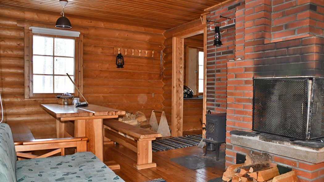 Inne i huset finns en öppen spis, en soffa och ett bord med bänkar. Det finns oljelampor, en korg med träd och en matta på golvet.
